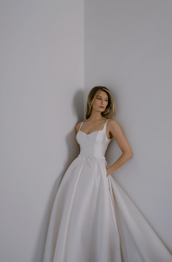 PEARLA takes the classic fairytale princess dress and gives it a contemporary twist. Crafted from top-of-the-line Mikado Silk, this gown is structured and smooth, which makes it appear as if it’s floating around the bride. PEARLA features a romantic sweetheart neckline, a sexy low back, deep folds throughout the skirt, and a naïve bow to embellish the delicate belt.