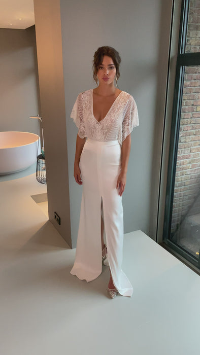 This two-piece wedding gown is fit for a Goddess. The cascading top is crafted from romantic, ultra-feminine lace which flatters all body types, while the fitted skirt features a central slit and beautiful rich satin. The result is a chic and romantic bridal gown, with classic elements reimagined for the contemporary bride.