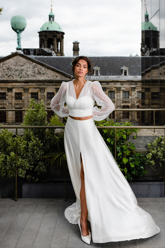 This modern contemporary 3-piece wedding dress is a vision in pure silk. LOLA is an elegant architectural dress comprised of a breezy slit skirt and form-fitting silk top, draped with an eye-catching tulle bolero. The gorgeous bolero is adorned with 3D flowers and tapers at the wrist. 