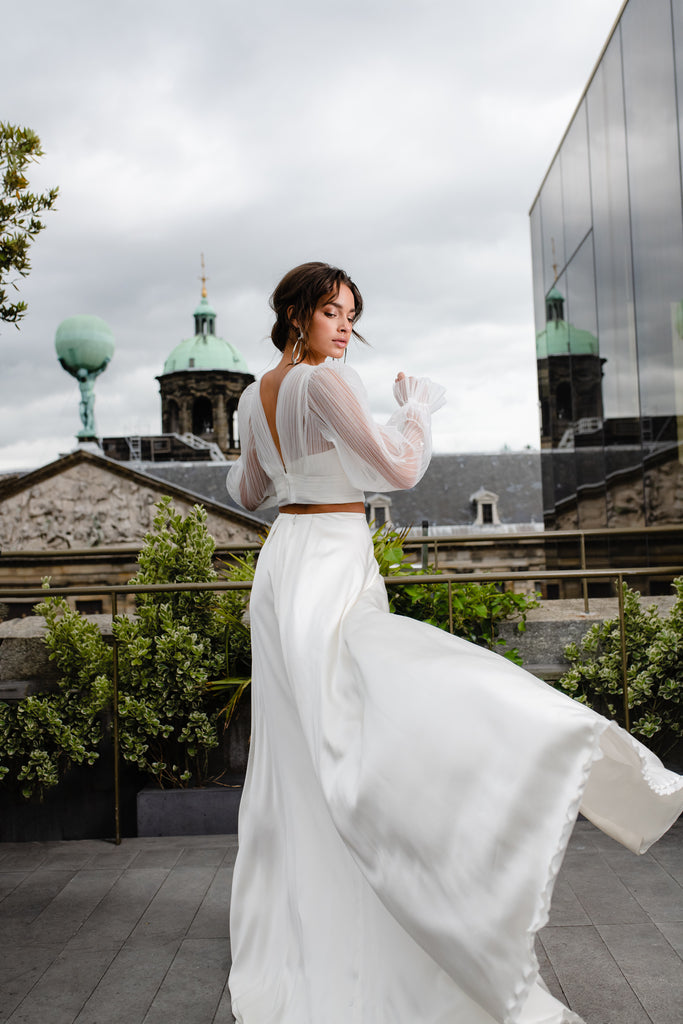 This modern contemporary 3-piece wedding dress is a vision in pure silk. LOLA is an elegant architectural dress comprised of a breezy slit skirt and form-fitting silk top, draped with an eye-catching tulle bolero. The gorgeous bolero is adorned with 3D flowers and tapers at the wrist. 