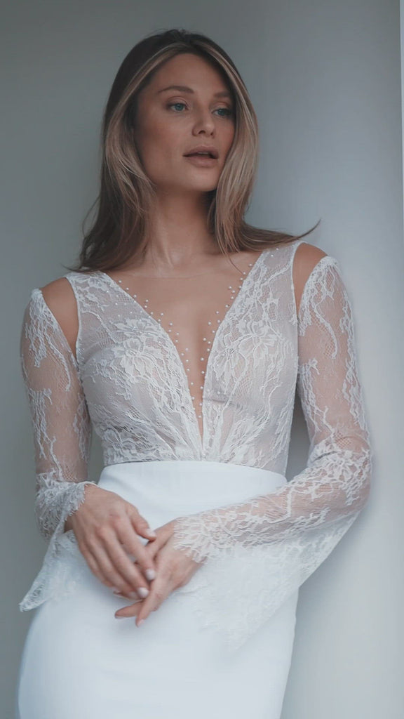 IYAR is a sexy and sophisticated Wedding Dress with a classic cut. The deep V-neckline is embellished with floating pearls. The gentle lace top features a peek-a-boo cold shoulder that reveals some extra skin. The long chiffon skirt boasts an elegant triangle train. The look is finished off with hand-sewn buttons that run down the low-cut back.