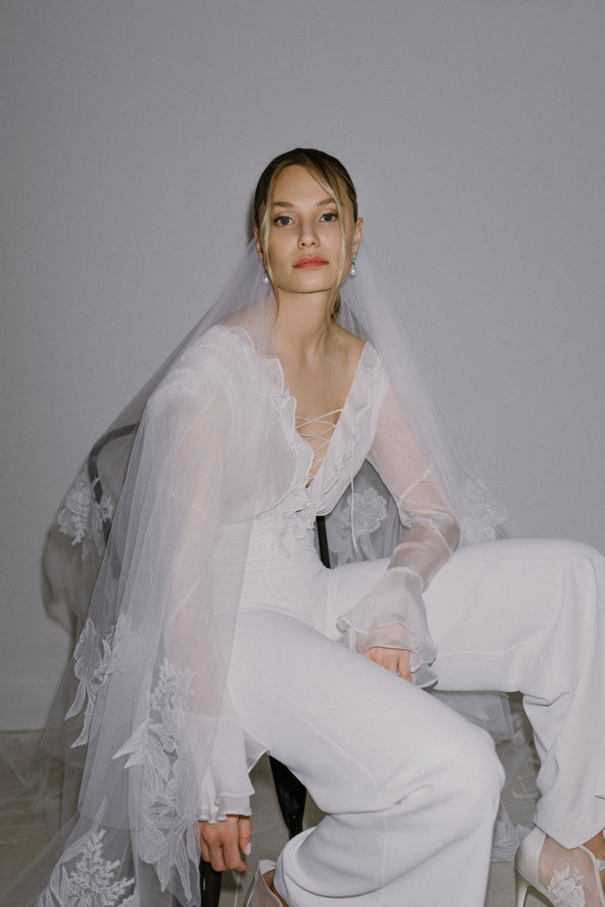 DIDI is a stylish bridal jumpsuit crafted in silk and chiffon. The lovely top features a breezy volan detail, a playful lace-up deep V-neckline, and breezy chiffon sleeves. The silk pants are smooth and create enchanting movement, designed to keep you dancing all night long!