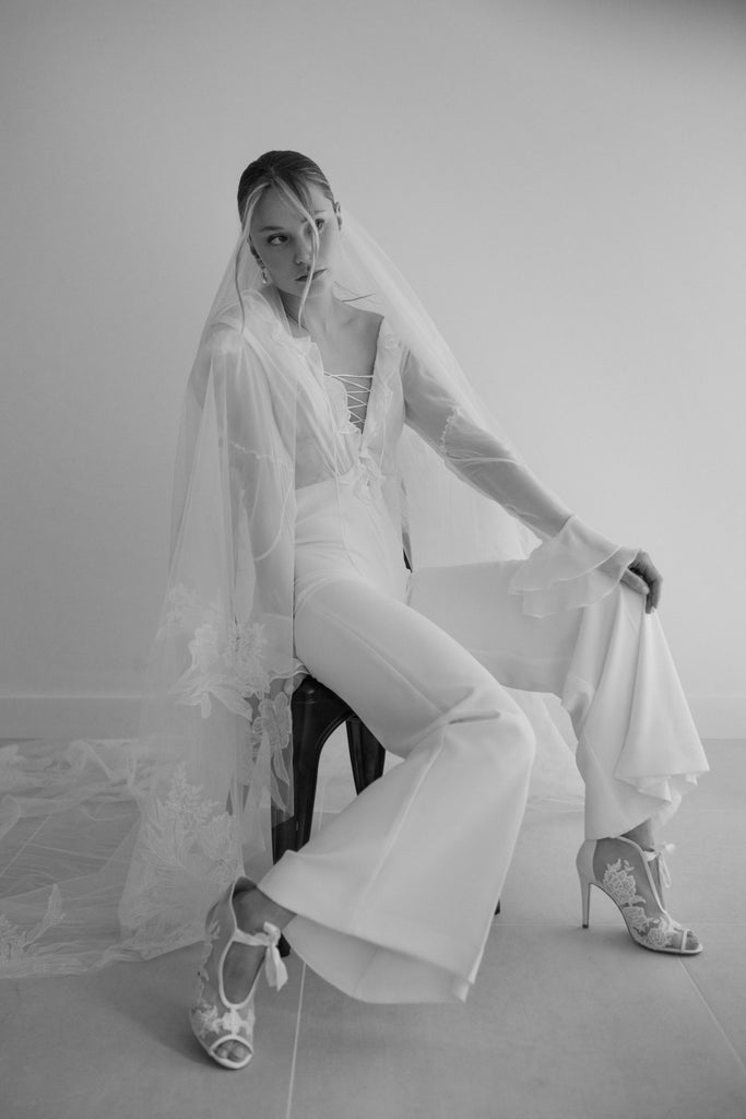 DIDI is a stylish bridal jumpsuit crafted in silk and chiffon. The lovely top features a breezy volan detail, a playful lace-up deep V-neckline, and breezy chiffon sleeves. The silk pants are smooth and create enchanting movement, designed to keep you dancing all night long!