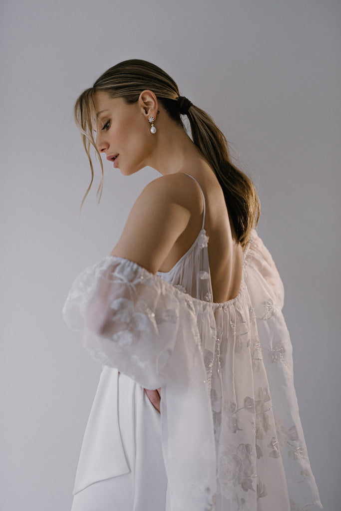 It’s always the quiet ones that get you: You’ll surely fall in love with FEFFER’s soft allure. This bridal gown features a handcrafted draped satin skirt with a flattering high waist and side slit. The deep plunge top is crafted in stunning draped tulle and is embellished with soft 3D lace flowers, for a dreamy finish. 