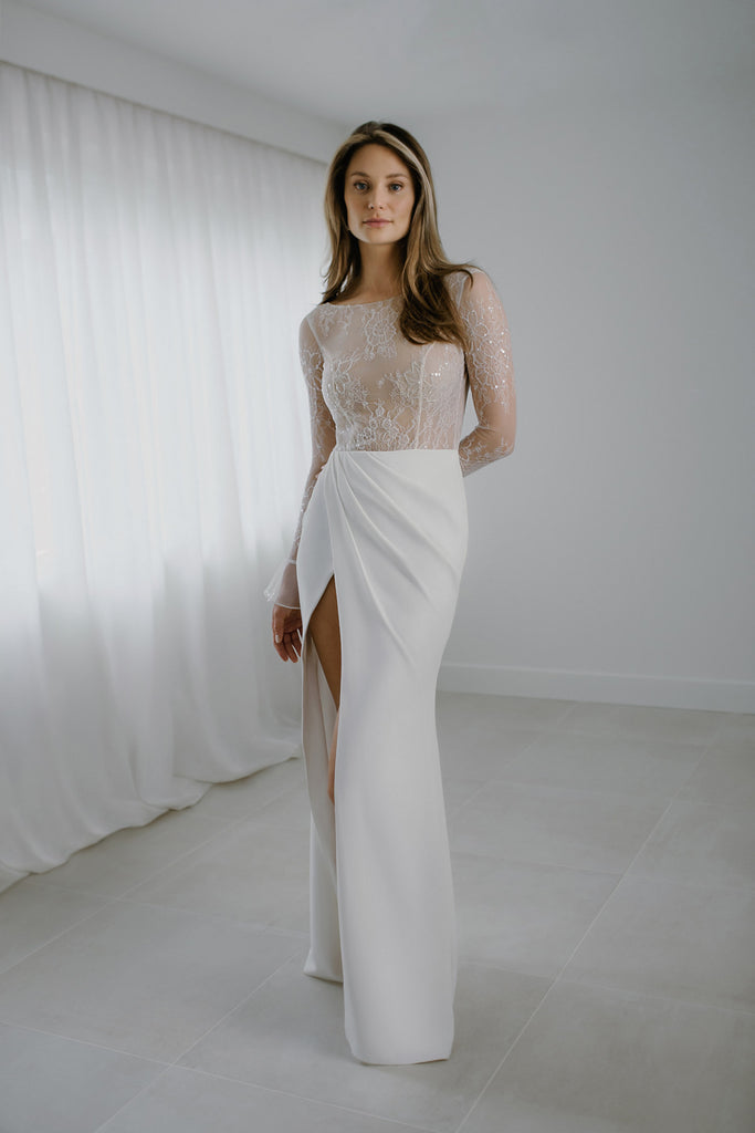 YULI is a modern beauty, with a crisp and clean appearance. The top of this bridal dress is crafted in beautiful 3D lace that sparkles lightly, and the sleeves are tapered with a romantic Volan. The draped folded skirt features a seductive side slit, and button details that run down the back. YULI can be layered with a matching sparkly 3D lace overskirt that gives this bridal gown a dramatic and alluring train.