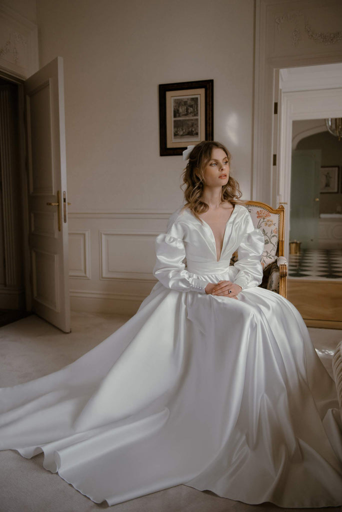 This ultra-romantic vision is made entirely from luxurious satin. LUCY features pompous sleeves, a cloche skirt, and a wide structured belt which gives the dress a flattering and gathered shape.   This dress is reimagined romantic nostalgia, fit for the fashion-forward bride who’s inspired by timeless tales of love.