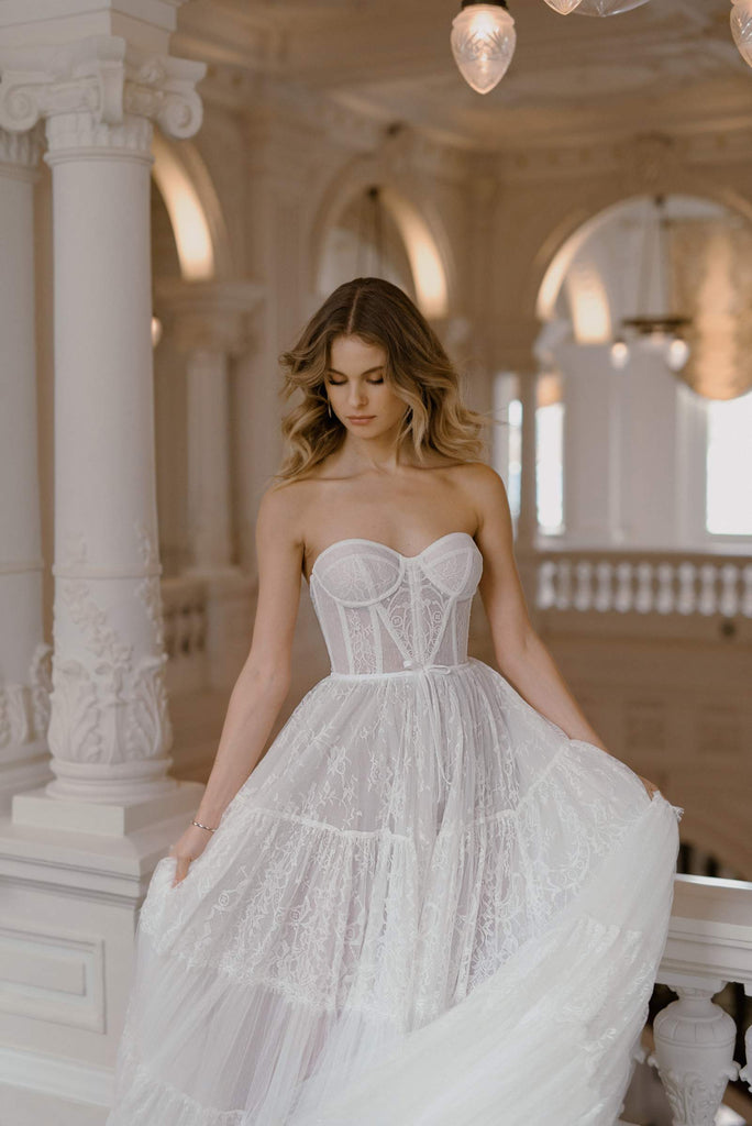 The STELLA Wedding Dress is crafted with 70 meters of tulle and gathered French lace. A gentle structured corset rests teasingly on top of the 5-tiered boho skirt.   STELLA is truly an alluring vision, brought to life with elite craftsmanship. This gown is the perfect choice for a bride who appreciates couture fashion.